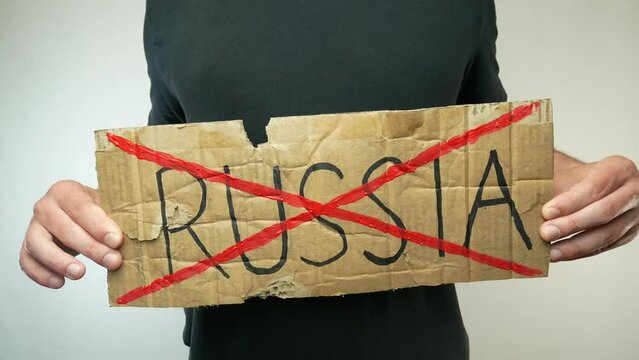 A man in a black t-shirt holds a cardboard sign with the word russia