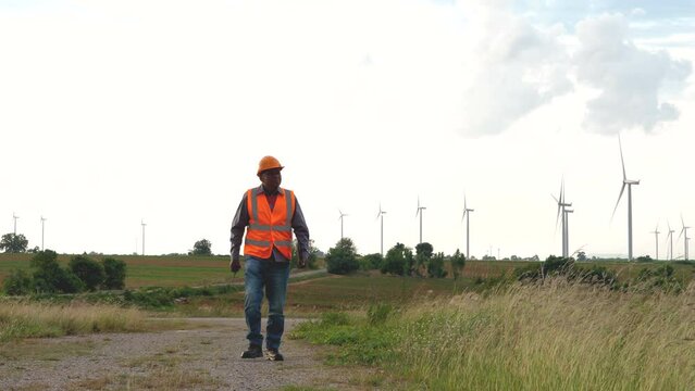 Senior engineer worker man walking in background wind turbines field, green environmental energy. windmill power station.
