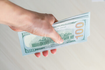 A stack of one hundred dollar bills is held by a woman's hand. A stack of one hundred dollar bills in a hand on a light background.