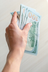 A stack of one hundred dollar bills is held by a woman's hand. A stack of one hundred dollar bills in a hand on a light background.