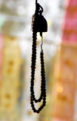 A brown wooden rosary is hung from a golden bronze bell on a blurred background.