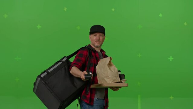 Caucasian male courier passing a box of pizza on green screen chroma key background. Man hold wireless bank payment POS terminal to process acquire credit card payment. Copy space mock up advertising