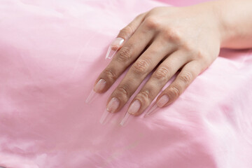 hand of a young woman placed on a pink blanket, with transparent false nails ready for manicuring