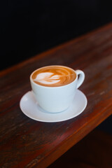 Delicious beautiful cappuccino in a white bowl on a wooden table. Atmospheric photo of coffee on a dark background