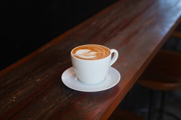 Delicious cappuccino in a white cup on a wooden background. Aromatic coffee on a dark background