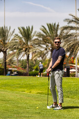 Young man golfer standing on golf course in sportswear and sunglasses, teeing golf club training at...