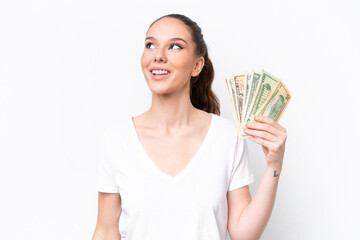 Young caucasian woman taking a lot of money isolated on white background thinking an idea while looking up