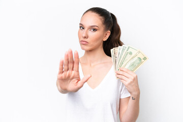 Young caucasian woman taking a lot of money isolated on white background making stop gesture