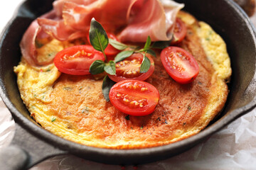 Omelette with tomato and prosciutto on a cast iron pan. Fresh vegetarian breakfast, close-up.