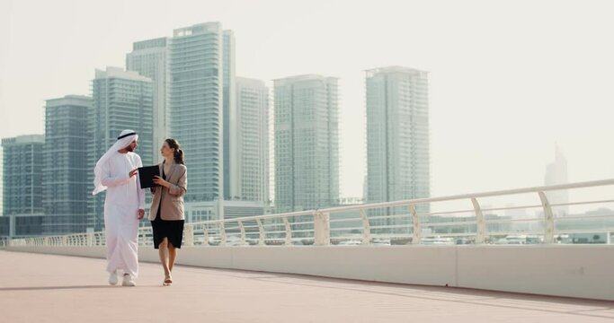 A business woman of European appearance discusses documents with her Arab partners walking down the street of a modern city