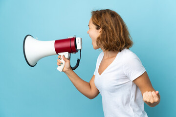 Young Georgian woman isolated on blue background shouting through a megaphone to announce something in lateral position