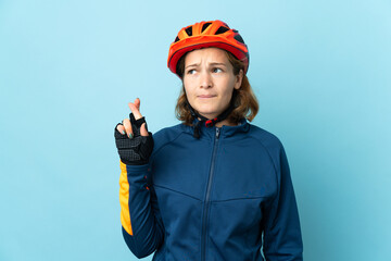 Young cyclist woman isolated on blue background with fingers crossing and wishing the best