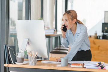Young adult Asian businesswoman, secretary, sales manager, business consultant, engaging in a phone conversation with a client at the office.