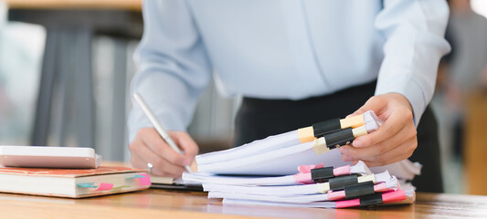 A businesswoman is sifting through stacks of paper files and folders that contain both incomplete and completed documents. Selective focus - obrazy, fototapety, plakaty