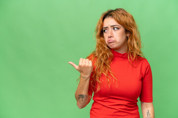 Young caucasian woman isolated on green screen chroma key background unhappy and pointing to the side