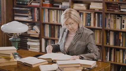 Senior female scientist doing research at the library, reading books, her hobby