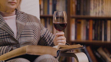Senior woman reading a book and drinking wine in a home office, recreation