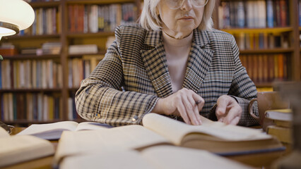 Concentrated mature woman reading an article in a scientific book, making notes