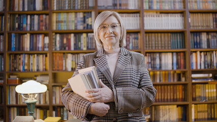 Portrait of a smiling woman professor holding books in a library, doing research