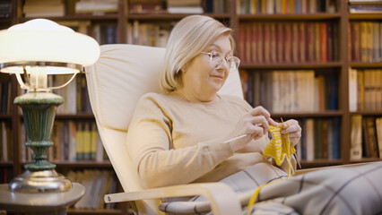Woman in her 50s knitting in her cozy apartment, handmade clothes, enjoying her hobby