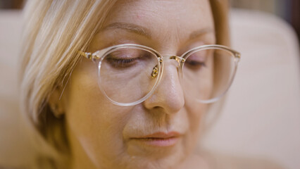 Close-up of the face of a concentrated blond woman in glasses, looking down, doing her hobby