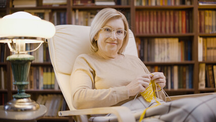 Portrait of a smiling mature woman knitting in the evening, entertainment, hobby