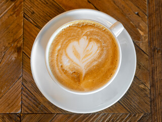 A cup of cappuccino with foam decoration on a wooden table