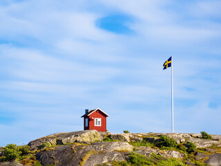 Isolated red swedish wooden cottage and swedish flag on the top of the hill of the island of Vrango in Sweden, near the Gothenburg