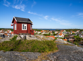 Fototapeta na wymiar Red swedish wooden cottage on the top of the hill and a view at the cityscape of the island Vrango in Sweden, near the Gothenburg