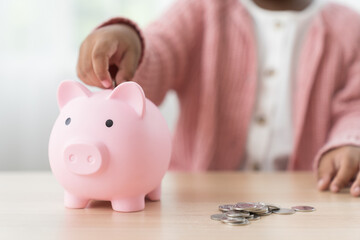 Saving and banking money concept. Girl kid putting money into the piggybank. African American girl kid inserting a coin in a piggy bank. Kid investment for future concept
