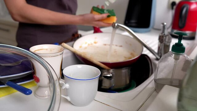 young woman washes dirty dishes in frying pan
