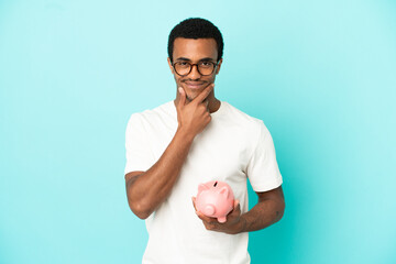 African American handsome man holding a piggybank over isolated blue background thinking