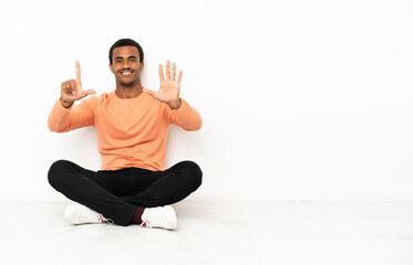 African American man sitting on the floor over isolated copyspace background counting seven with fingers