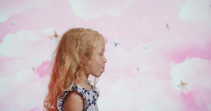 Girl in vanilla sky with stars blows bubblegum bubble and it pops in her face. Small girl in pink world chewing bubble gum