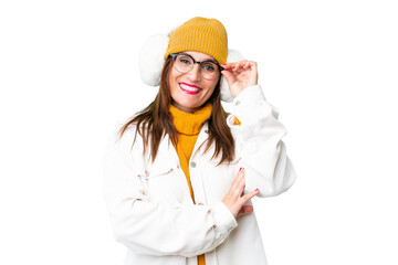 Middle age woman wearing winter muffs over isolated chroma key background with glasses and happy