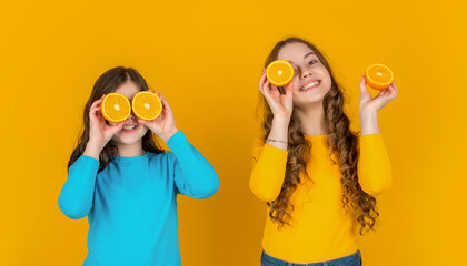 glad teen girls hold orange fruit on yellow background
