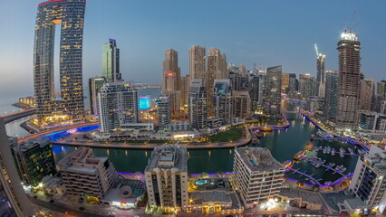 Fototapeta premium Panoramic view of Dubai Marina with several boat and yachts parked in harbor and skyscrapers around canal aerial day to night timelapse.