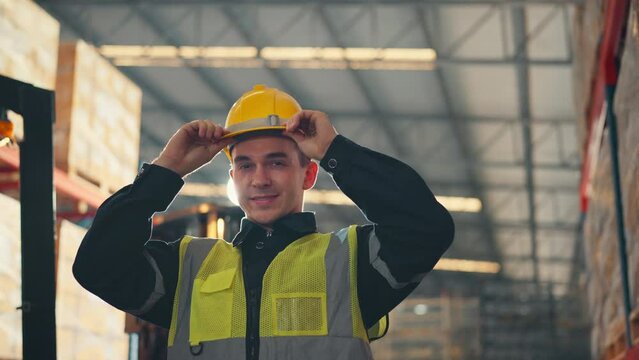 Happy professional worker puts on hard hat and looking at camera and smiling in the background warehouse with shelves full of delivery goods. Logistics, Delivery, and Distribution center.