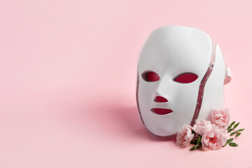 Health and beauty of the face. Cosmetic LED facial mask regenerative treatment on a pink background...