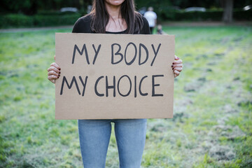 Woman holds up a sign that reads - My body my choice - in protest at an outdoor park