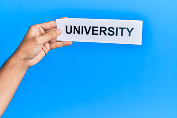 Hand of caucasian man holding paper with university word over isolated blue background