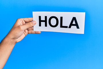 Hand of caucasian man holding paper with hola word over isolated blue background
