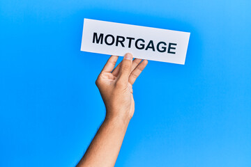 Hand of caucasian man holding paper with mortgage word over isolated blue background