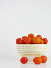 Fresh cherry tomatoes in a ceramic bowl and white background. Vertical shot and copy space.
