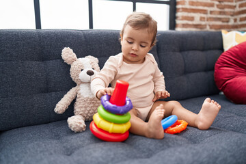 Adorable hispanic baby playing with hoops game sitting on sofa at home