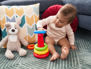 Naklejka premium Adorable hispanic baby playing with hoops game sitting on floor at home