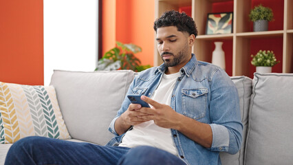 African american man using smartphone sitting on sofa at home