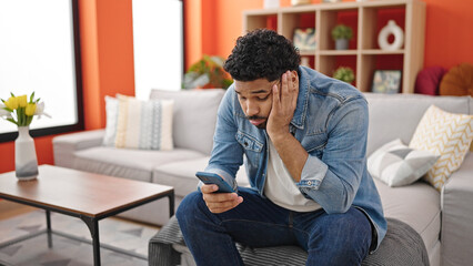 African american man using smartphone with worried expression at home