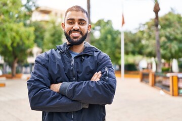 Young hispanic man standing with arms crossed gesture at park