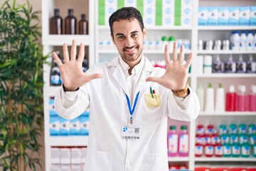 Handsome hispanic man working at pharmacy drugstore showing and pointing up with fingers number ten while smiling confident and happy.